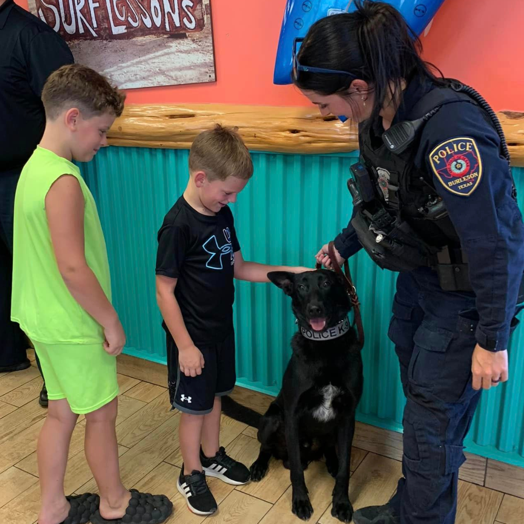 Photo of K9 Sonic receiving pets from two young boys at Shaved Ice with a Cop event 